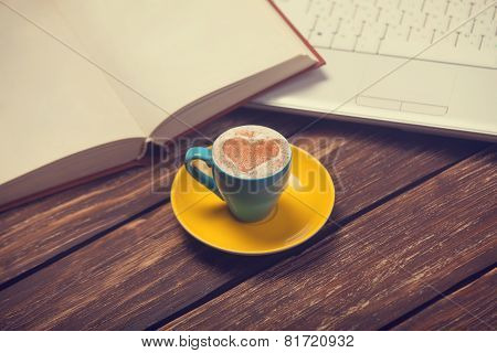 Cup Of Coffee With Heart Shape And Notbook On Wooden Table.