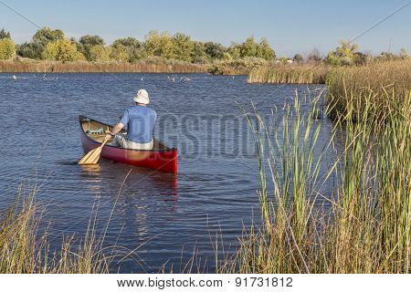 senior male paddler paddling a red canoe on a calm lake, Riverbend Ponds Natural Area, Fort Collins, Colorado