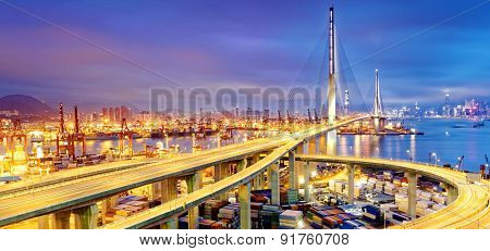 Container Cargo freight ship with working crane bridge in shipyard under Stonecutters highway bridge at sunset for Logistic Import Export, Hong kong