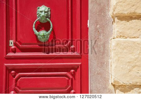 A wood red door with lionhead knob and keylock close to a yellow wall