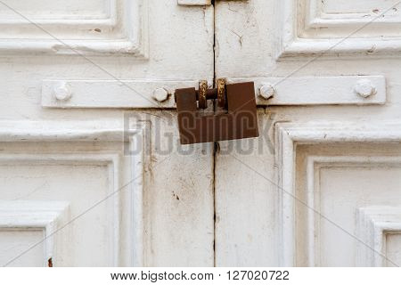 A withe wood door closed with a weathered rusty lock