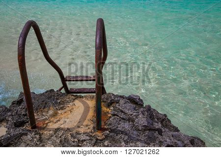 Rusty stairs on rocks to pool-like sea waters