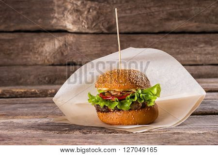 Fresh burger on a stick. Beefburger on wooden background. Juicy beef and fresh vegetables. Well-made burger in bistro.