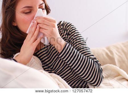Portrait of a sick woman blowing her nose while sitting on the sofa.