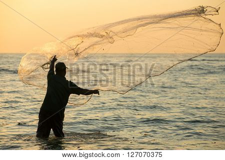 Silhouette of the unidentified Indian fisherman throwing net in sea on sunset in Fort Kochi, India.
