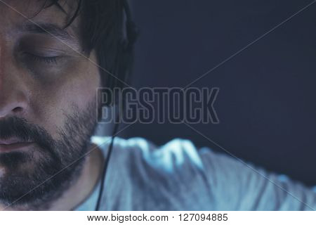 Man listening to music with eyes closed adult unshaven male enjoying favorite song on headphones half face low key portrait