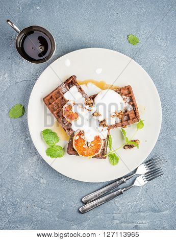 Belgian soft waffles with blood orange, cream, marple syrup and mint  on white plates over concrete textured background. Top view, vertical