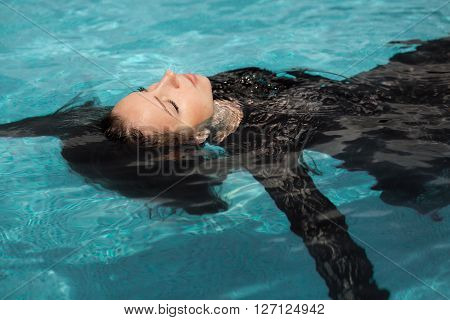 Portrait of the beautiful woman in black dress floating in blue water