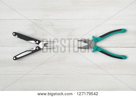 Simple pliers and multitool on wooden surface. Improved construction tools. Everyday instruments and tools. Progress. Construction and Repair.