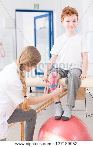 Happy cute little kid on physical therapy in a clinic. Young pretty physiotherapist taking care of boy