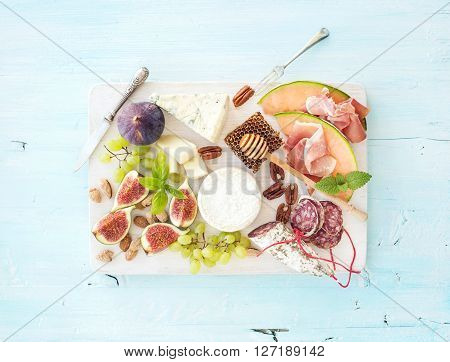 Wine and snack set. Figs, grapes, nuts, cheese variety, meat appetizers and herbs on light blue background, top view