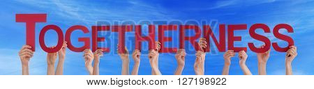 Many Caucasian People And Hands Holding Red Straight Letters Or Characters Building The English Word Togetherness On Blue Sky