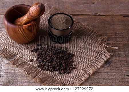 Black pepper corns and mill on wooden background