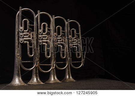 Four old brass wind instrument stand on a table on a black background