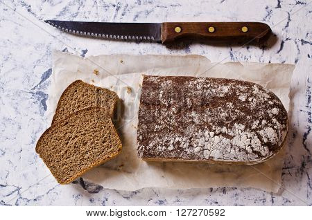 Cut loaf of rye bread on paper. Concrete background. Selective focus.