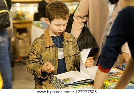 KYIV, UKRAINE - APR 21, 2016: Unidentified small boy reading colorful books at children area of the 6th Festival BOOK ARSENAL on April 21, 2016. Guests of fair were Lars Svendsen Vigdis Hjorth Etgar Keret