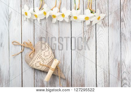 Narcissus flower, decorative heart on a light wooden background. Selective focus. Space for the text.