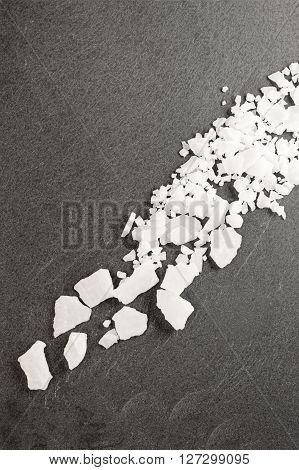 Top view of magnesium chloride flakes on a dark granite slate.