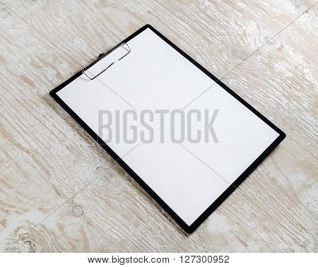 Photo of clipboard with a blank sheet of paper on light wooden background with plenty of copy space. Blank template for design presentations and portfolios.