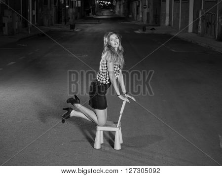 pretty blonde woman kneeling in child seat in the street at night