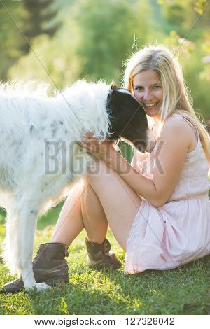 Happy blonde woman playing with her Russian wolfhound dog in garden