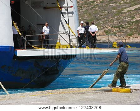 ISLAND OF SIFNOS, GREECE - AUGUST 24, 2007: Dock worker is pulling a rope while ship crew is standing on a docking platform of approaching ferry Agios Georgios, Ventouris Sea Lines.