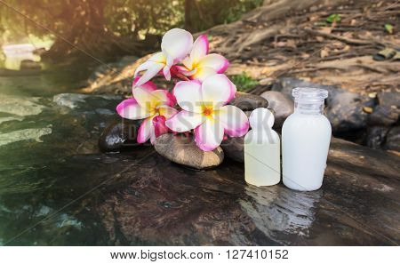 Mini set of bubble bath shower gel liquid with flowers and pebble on waterfall rock with natural water relaxing feeling background and copy sapce