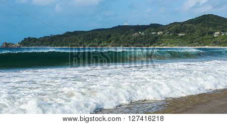 Byron Bay beach and waves in New South Wales, Australia with Cape Byron lighthouse in the background.