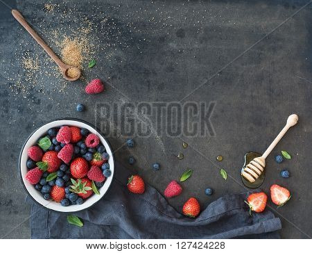 Berry frame with copy space on right. Strawberries, raspberries, blueberries and mint leaves, honey, cane sugar, dark grunge background, top view, copy space