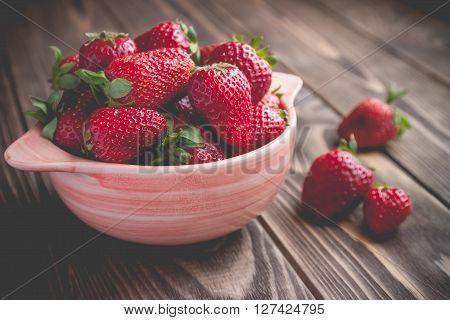 Fresh red strawberries on in a pink bowl on a rustic background in vintage style
