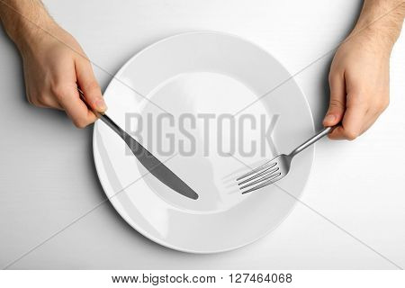 Male hands holding silver cutlery over plate, isolated on white