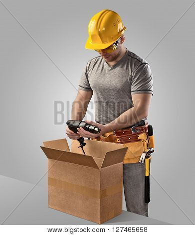 construction worker unpacks the box with delivery drill on gray background