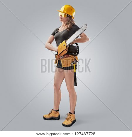 worker girl in a helmet with a chain saw on grey background