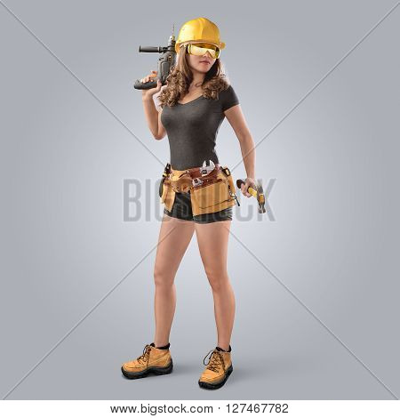 worker girl in a helmet with drill and hammer on grey background