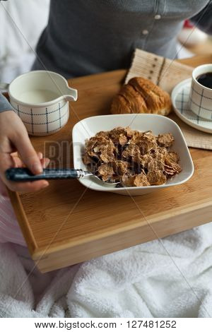 Healthy breakfast in bed served on tray with coffee, cornflakes, croissant and milk