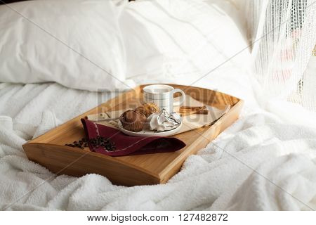 Sweet breakfast in bed served on tray with coffee and cupcakes. Sunny morning.