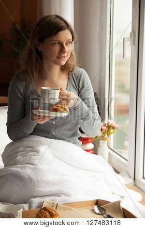 Healthy breakfast in bed served on tray with coffee, cornflakes, croissant and milk. Woman having her breakfast in bed.
