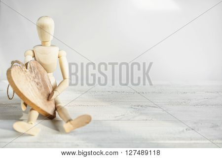The dummy sits on the board and holding a wooden heart.