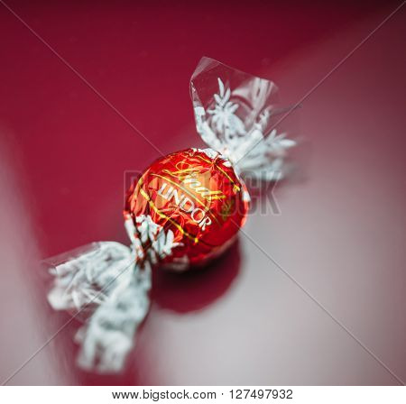 KILCHBERG SWITZERLAND - MARCH 20 2014: Lindt Lindor chocolate truffle on a red luxury silk background. Lindt is one one of the lastgest luxury chocolate and confectionery company worldwide with more than 30 factories worldwide