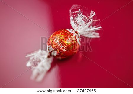 KILCHBERG SWITZERLAND - MARCH 20 2014: Lindt Lindor chocolate truffle on a red luxury silk background. Lindt is one one of the lastgest luxury chocolate and confectionery company worldwide with more than 30 factories worldwide