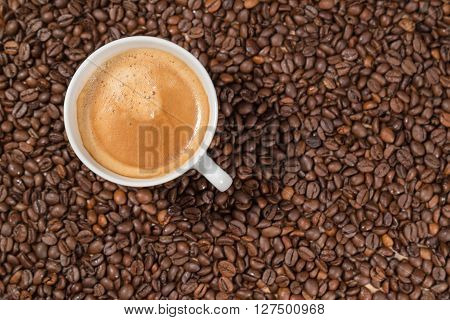 A cup of coffee is standing in a bunch of coffee beans.