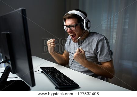 technology, gaming, entertainment, let's play and people concept - happy young man in eyeglasses with headset playing and winning computer game at home and streaming playthrough or walkthrough video