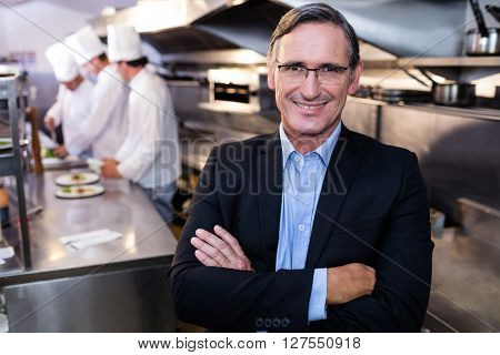 Male restaurant manager standing with arms crossed in commercial kitchen