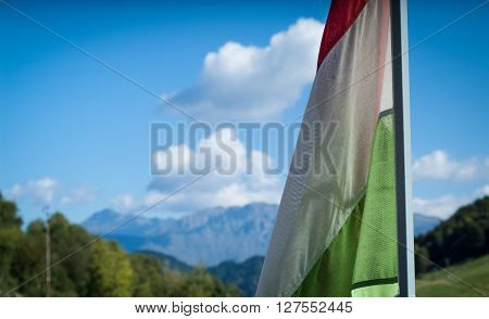 closeup photo of a wind-blown Italian flag with Piani d'Erna (part of the Alps) in the background