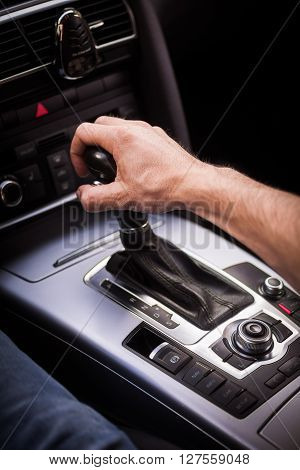 Detail of a hand pulling an automatic gear shifter in a new car.