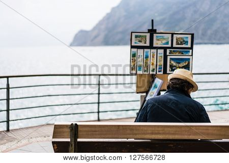 Monterosso Italy - Apr 8 2016: Unidentified street artist selling his landscape painting souvenirs by the ocean at Monterosso Cinque Terre Italy