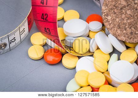 A bottle of diet pills with measuring tape on grey