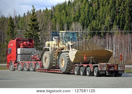 FORSSA, FINLAND - APRIL 23, 2016: Scania 164G semi truck transports a heavy duty Volvo L350F wheel loader as oversize load on lowboy trailer rear view.