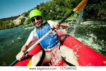 A happy entusiastic male in red inflatable canoe having a fun ride in calm waters of a river.