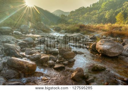 Beautiful Reshi River water flowing on rocks at dawn Sikkim India - sun rays at the background falling on water making spectacular view tinted image
